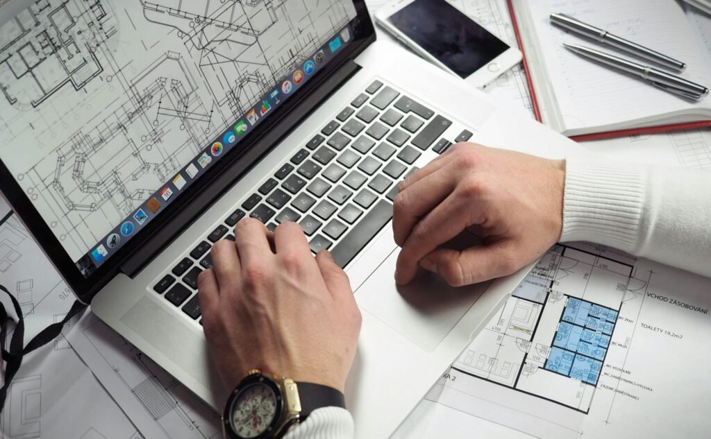Architect reviewing detailed floor plans and schematics on a laptop with a smartphone nearby.